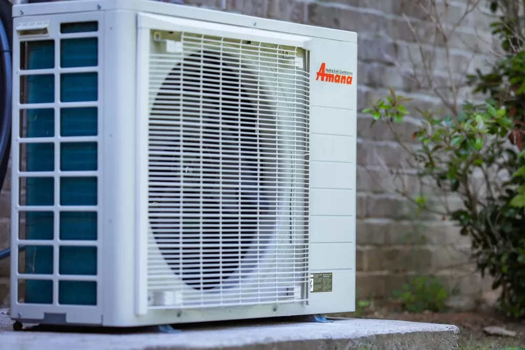 Amana S-Series heat pump outdoor unit installed on a concrete pad beside a home