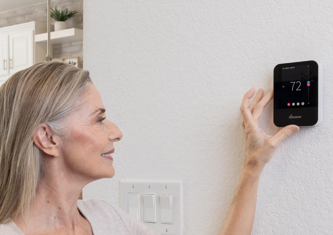 Homeowner adjusting an Amana Brand smart thermostat mounted on her living room wall